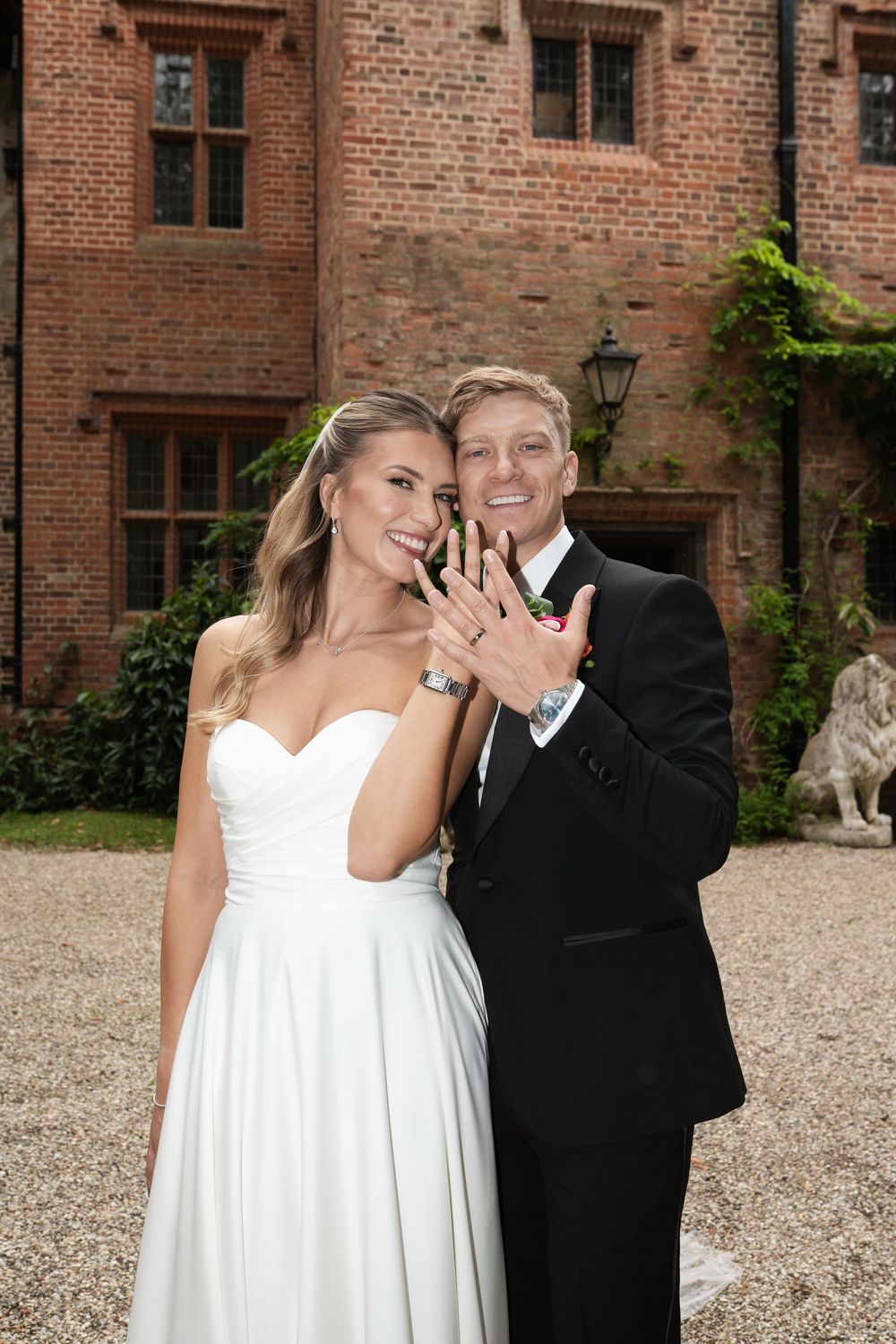 Happy couple shares joyful moments in white dress and black suit outside historic brick building.