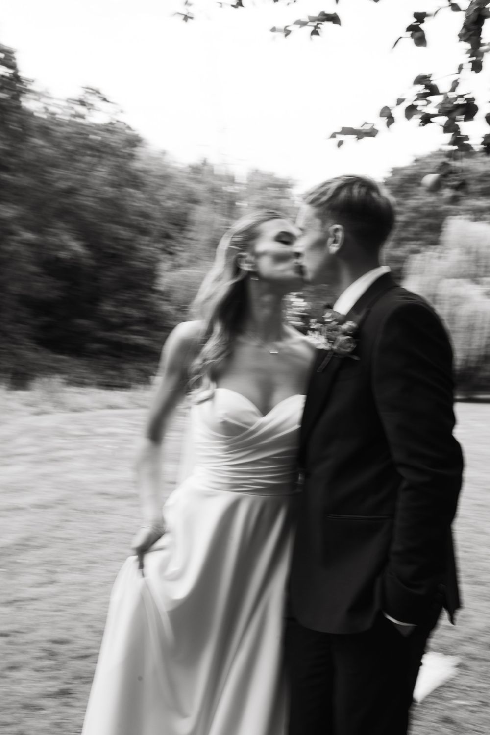 A couple in wedding attire dance together outdoors in a romantic black and white sequence.