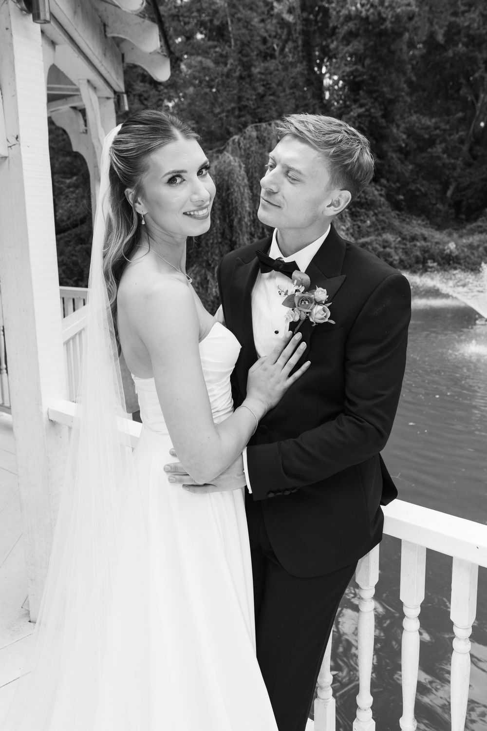 A bride and groom share playful, romantic poses together on their wedding day by white railings outdoors.