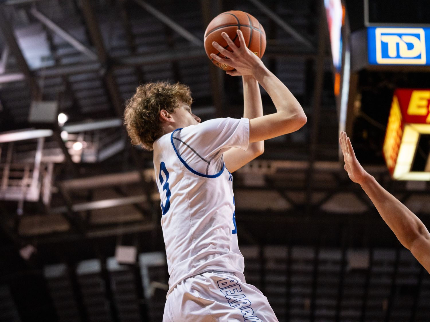 Basketball player in white jersey leaps for shot during indoor game.