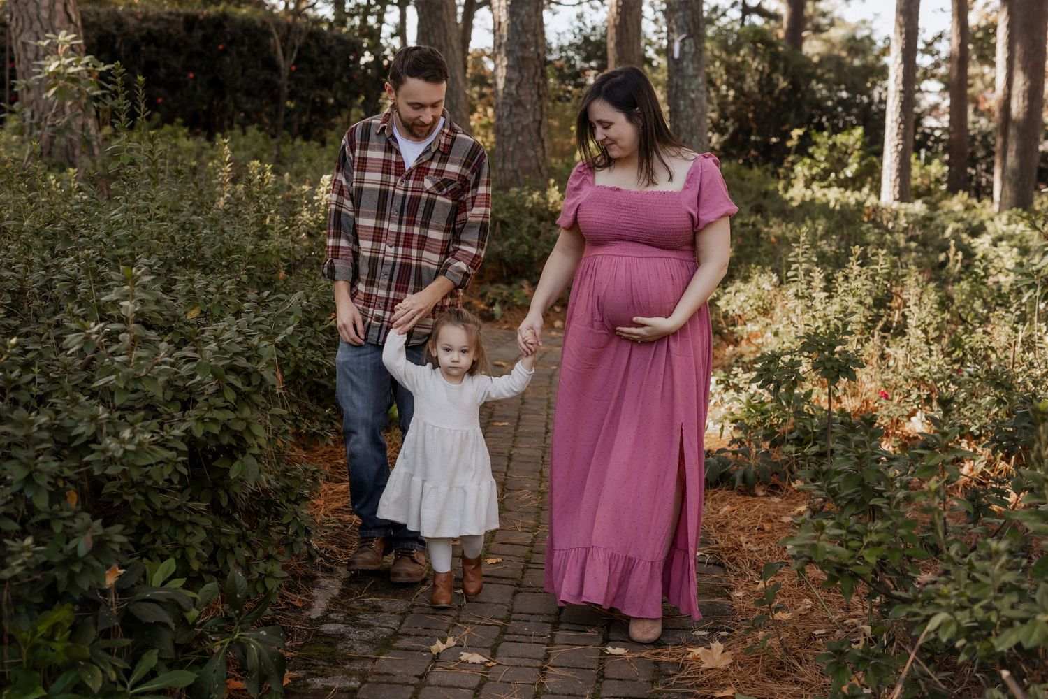 A family walks together on a garden path during golden hour as sunlight filters through trees.