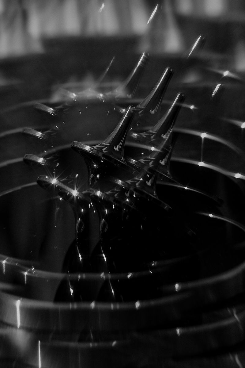 Black and white macro photo of ferrofluid spikes rising dramatically in a metallic container with liquid droplets.