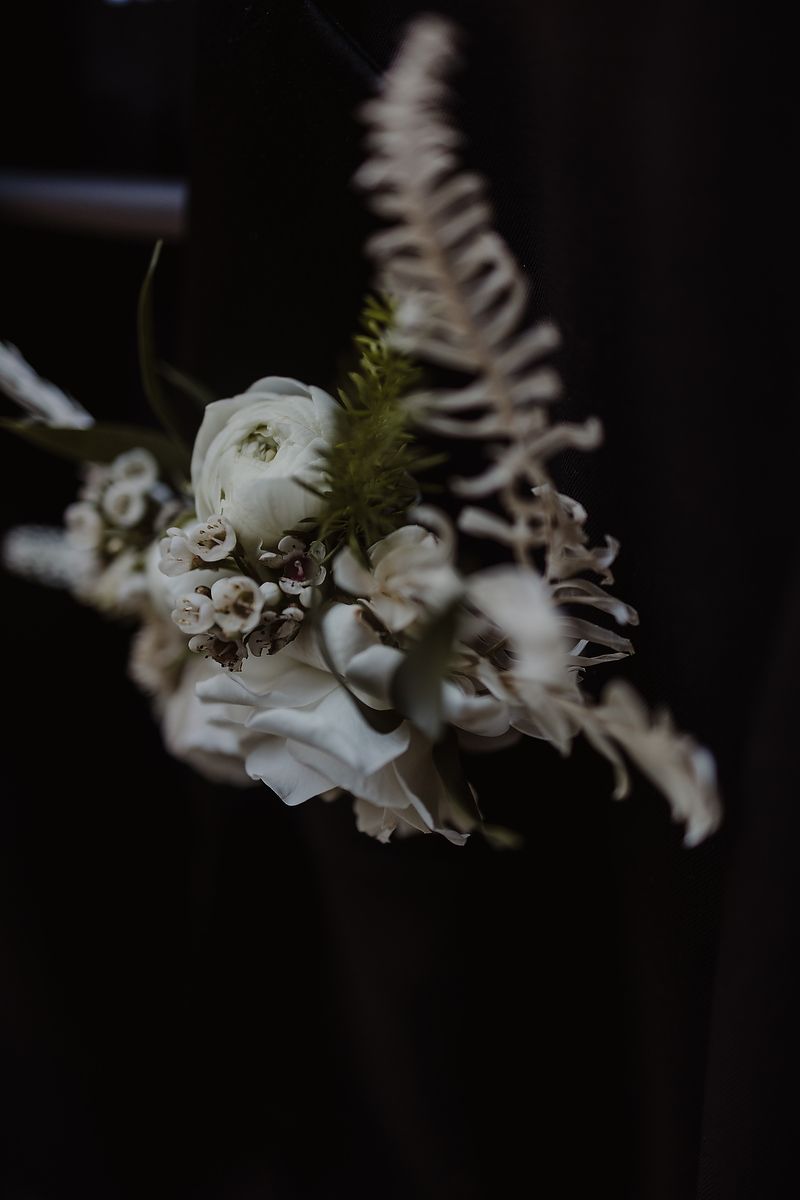 Elegant white floral bouquet with ranunculus, wax flowers, and fern against a dark moody background.