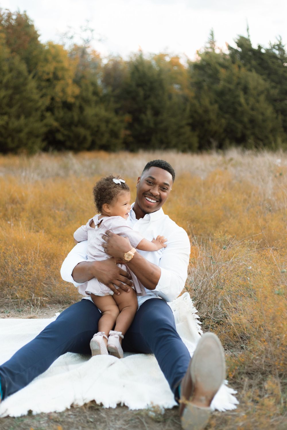 Joyful outdoor portrait on a blanket with adult and toddler against autumn foliage.