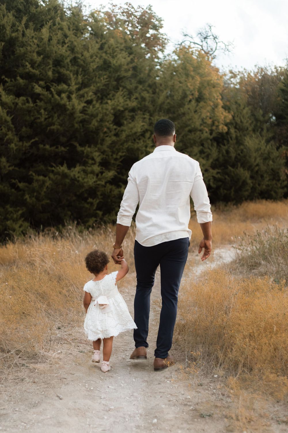 Adult and toddler holding hands while walking together on a nature path.