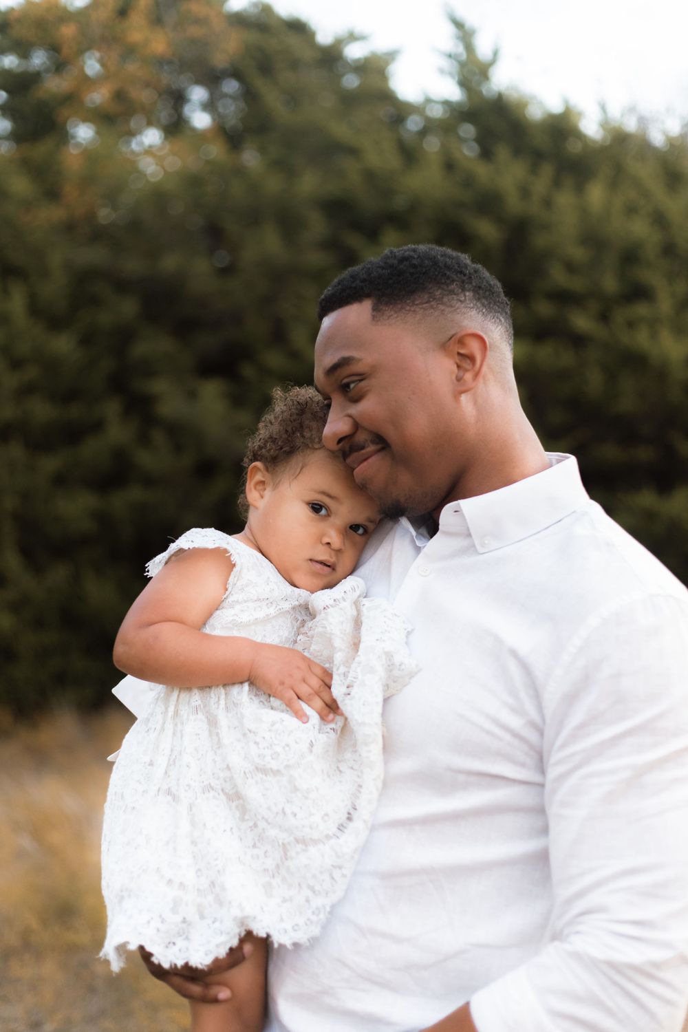 A tender moment between parent and child both dressed in white against a natural background.