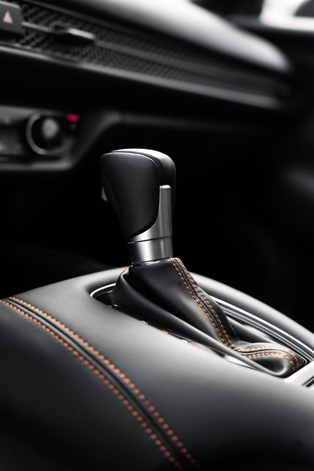 Black leather gear shifter with orange contrast stitching in modern car interior.Mtlshutter photography