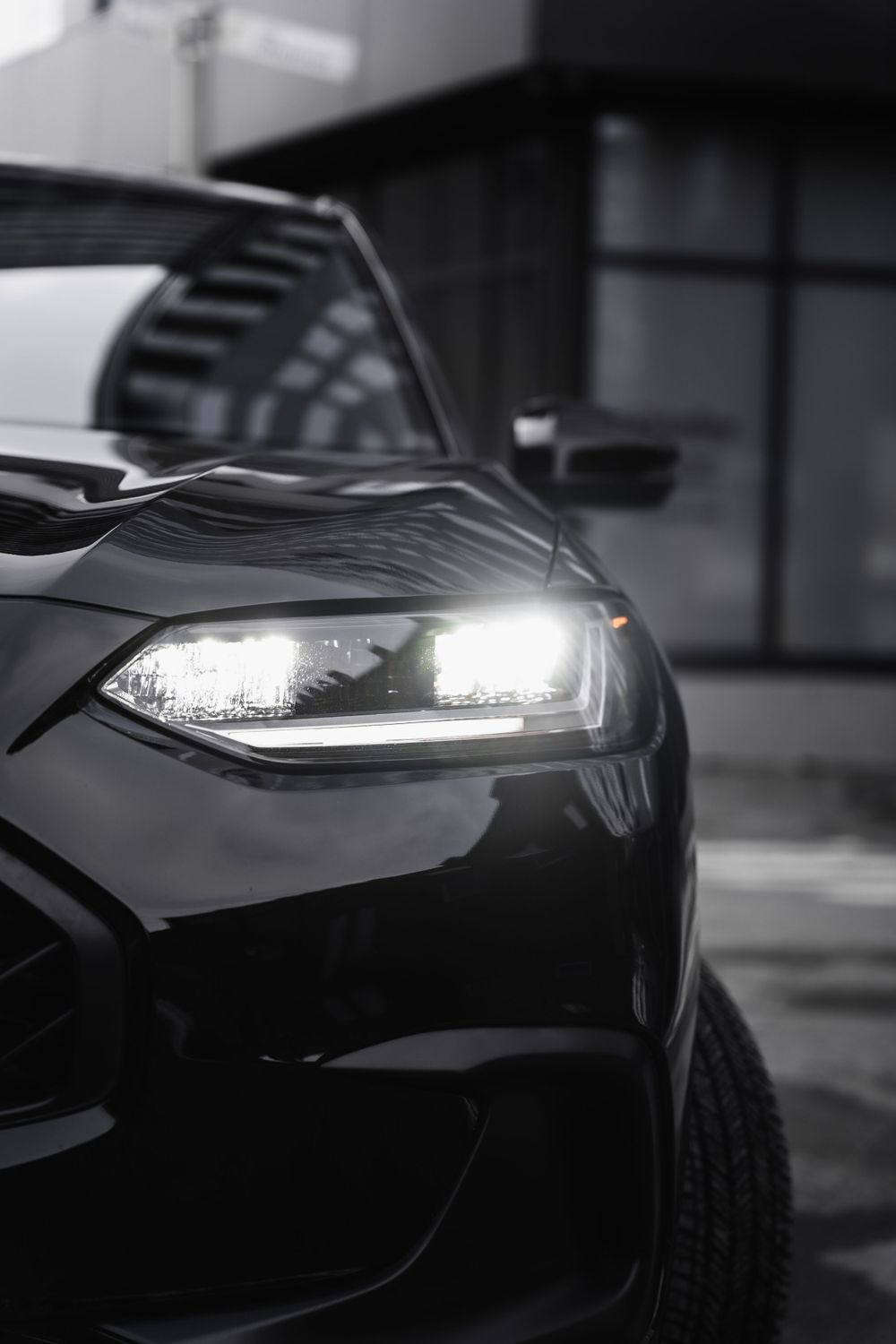 Front quarter view of LED headlight on black vehicle with urban background.Mtlshutter photography
