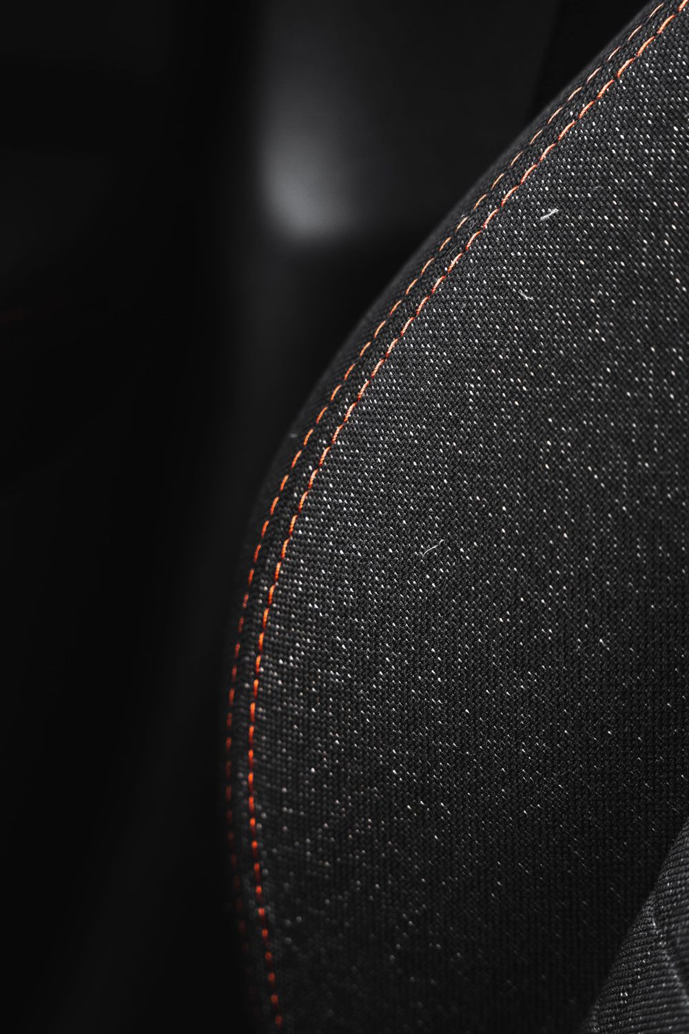 Black fabric car seat upholstery with orange contrast stitching detail.Mtlshutter photography