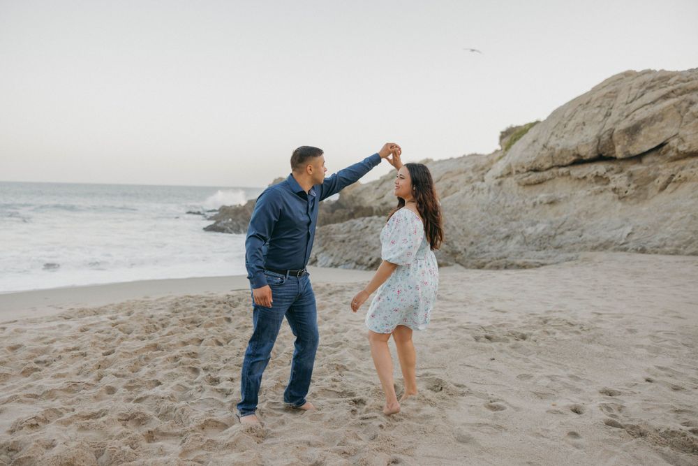 A playful dancing moment captured between a couple on a scenic beach.
