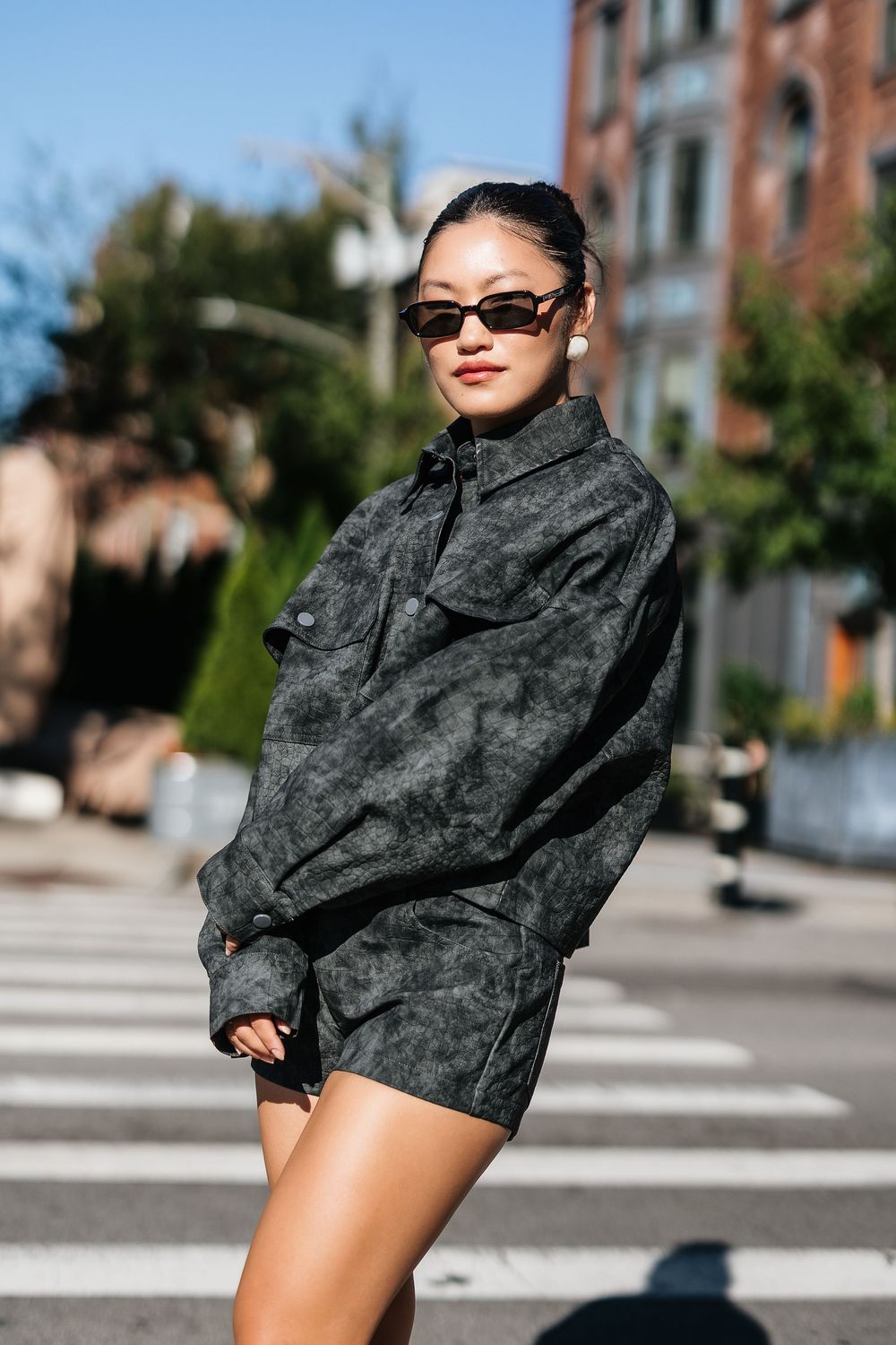 Woman in dark acid wash matching shorts set and sunglasses posing on a sunny urban street.