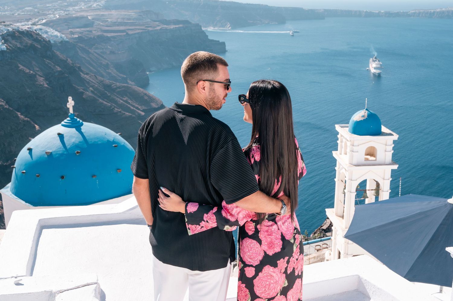 A couple admires the iconic blue domes and white architecture of Santorini while overlooking the Aegean Sea.