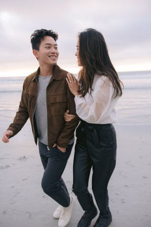 A couple shares a playful moment together while walking on the beach at sunset.