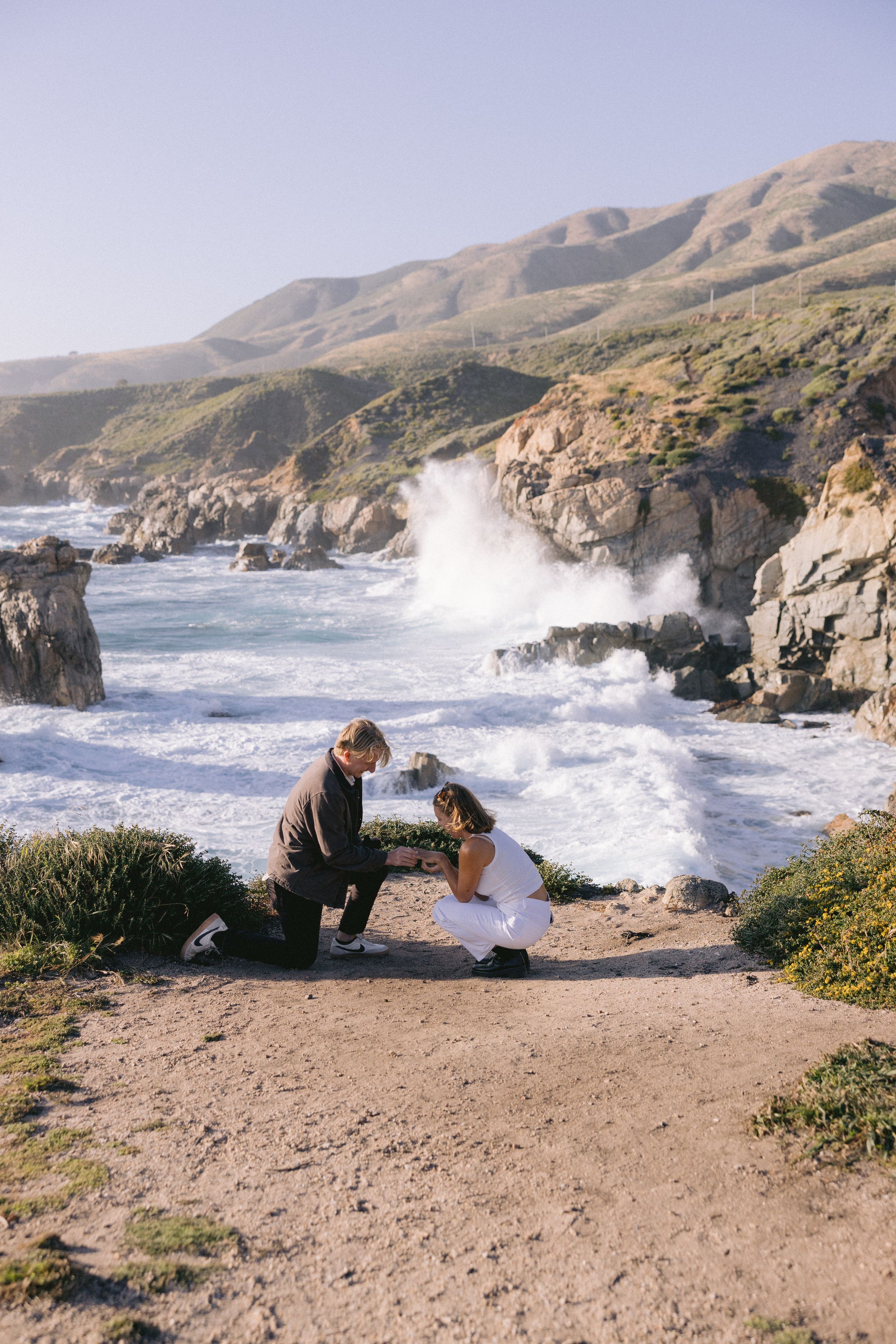 Dramatic coastal landscape shows waves crashing against rocky cliffs along Big Sur's rugged California coastline.