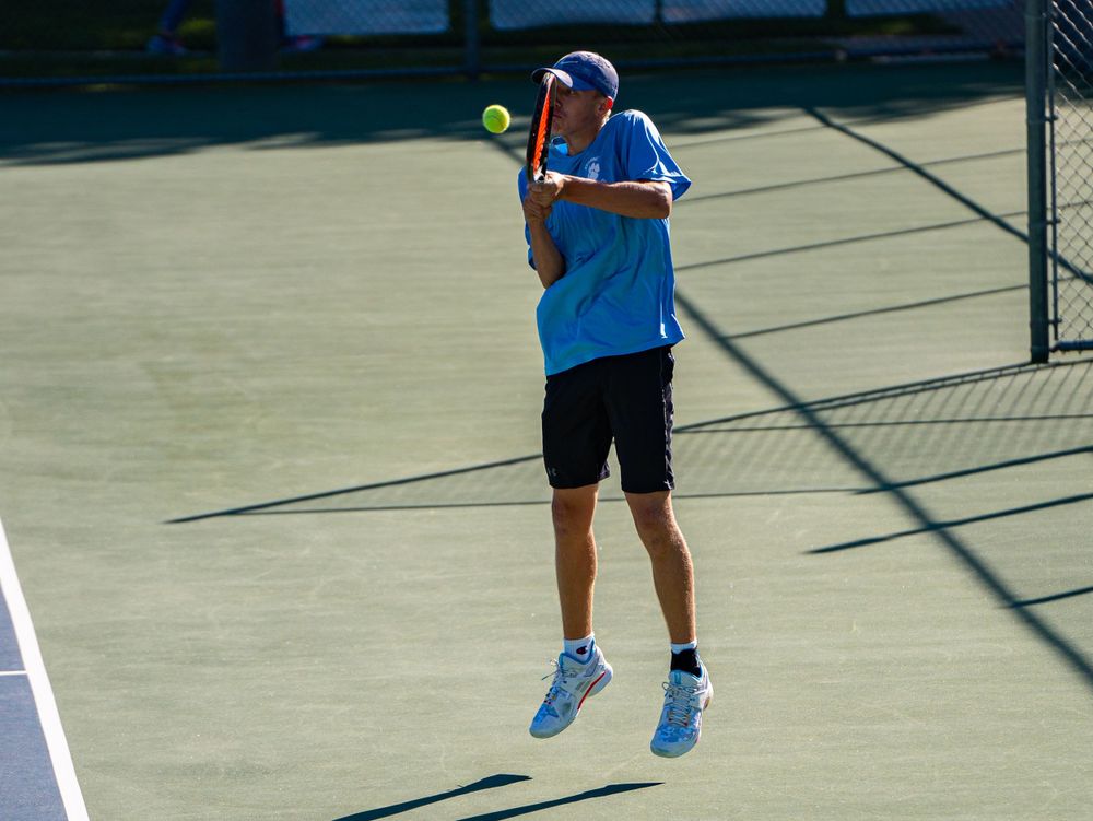 Tennis player executing jumping serve on outdoor court.