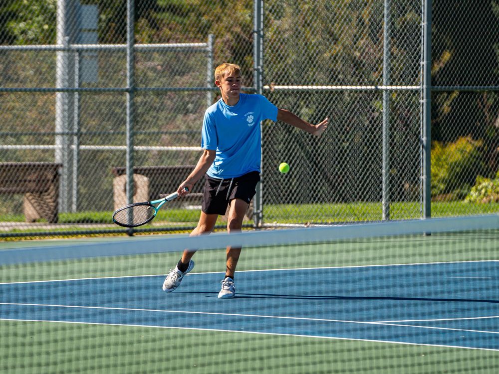 Player executing a powerful serve on a blue tennis court during daytime practice.