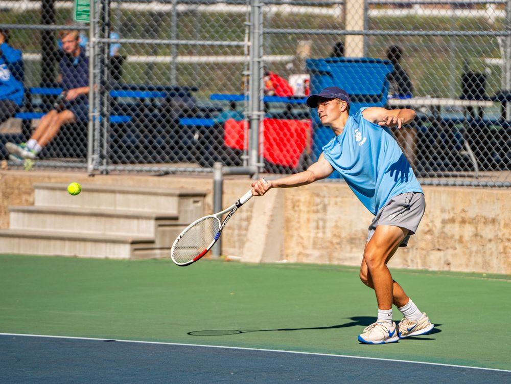Tennis player in blue shirt follows through on a powerful serve motion.