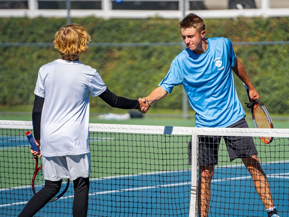 Tennis players shake hands across the net after match on blue court.