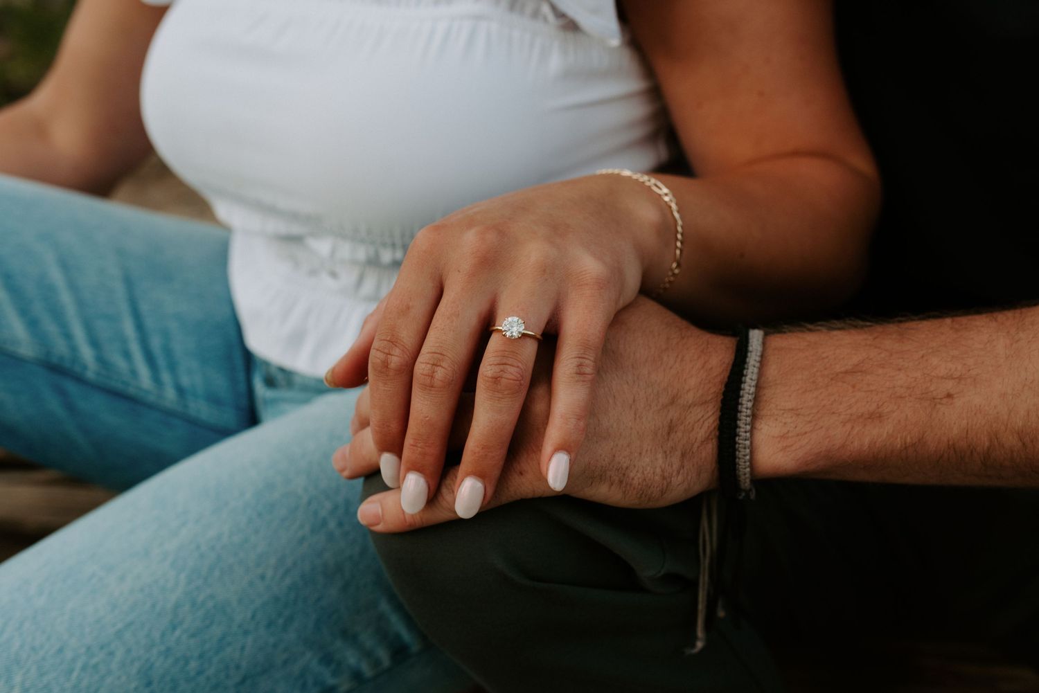 Couple's hands with engagement ring resting together on light blue fabric.