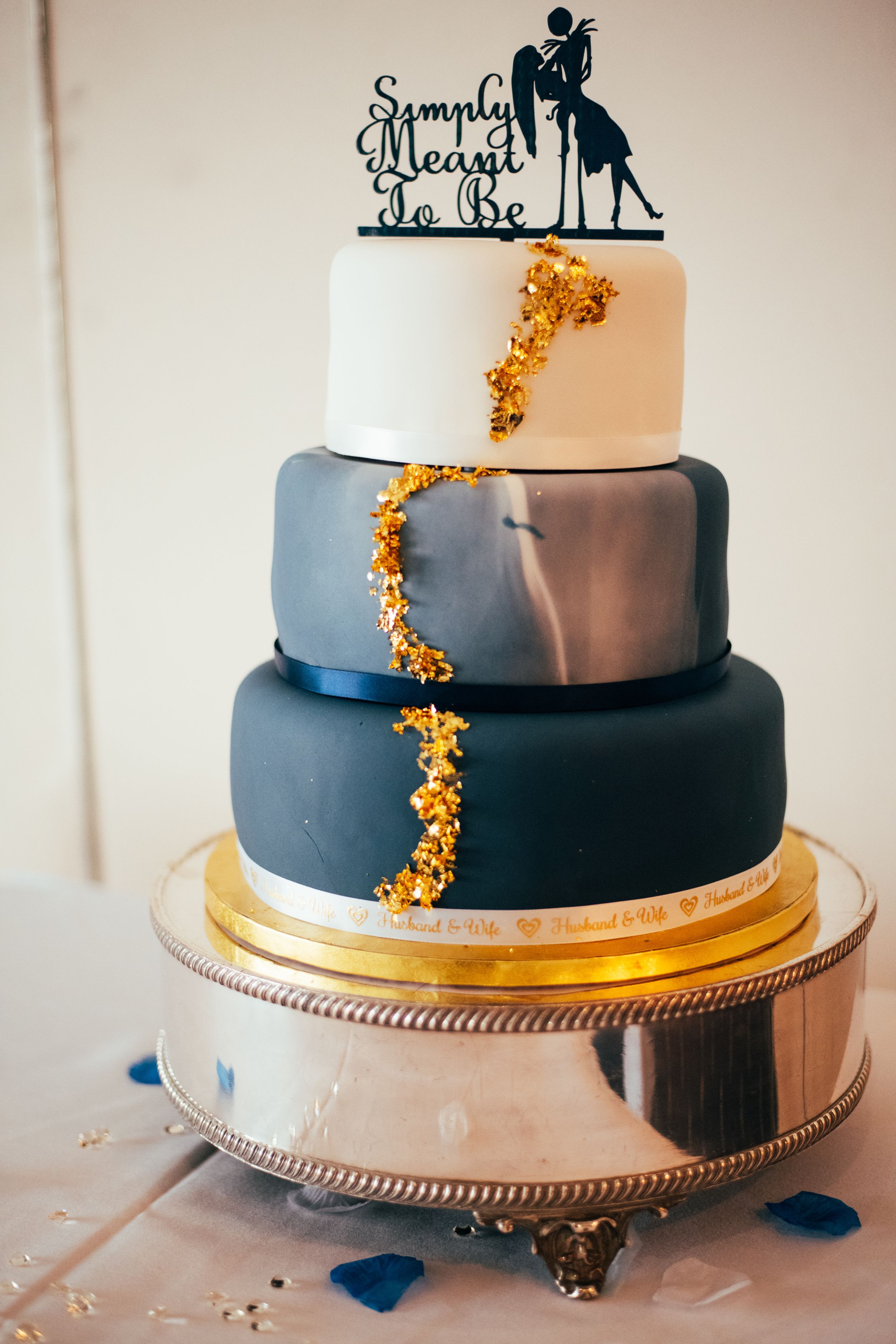 Three-tiered wedding cake decorated with navy blue ombre frosting and gold accents on a silver cake stand.