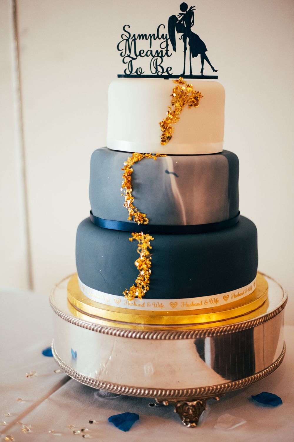 Three-tiered wedding cake decorated with navy blue ombre frosting and gold accents on a silver cake stand.