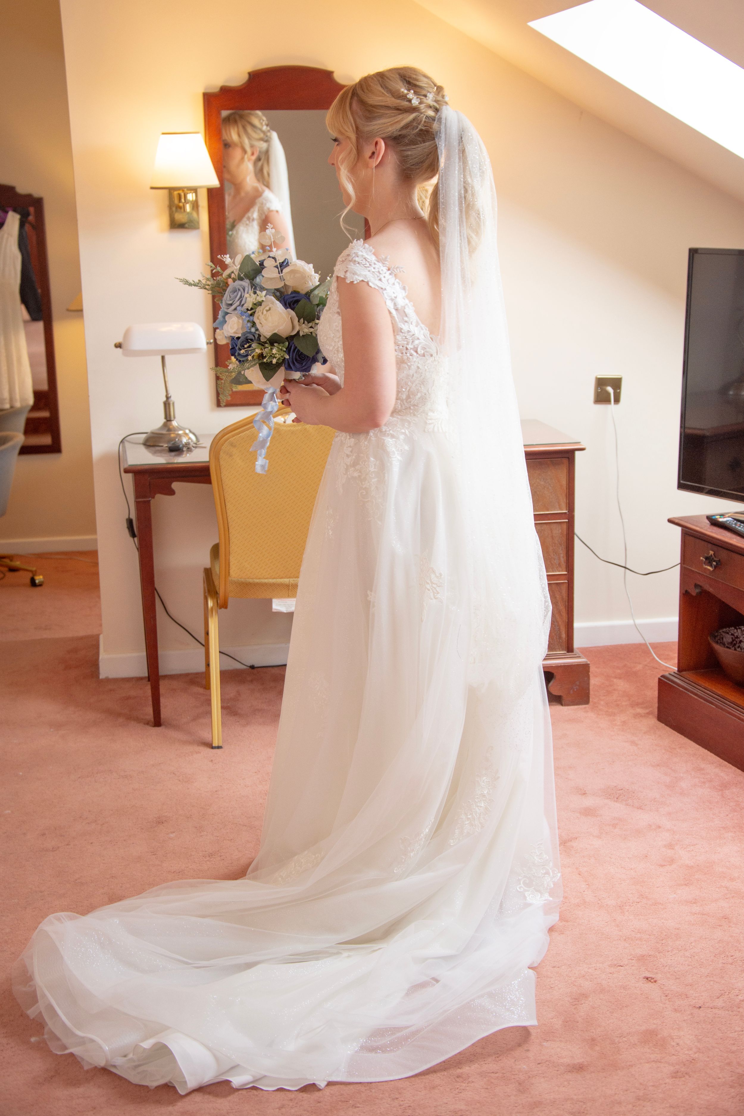 Elegant white lace wedding gown with long train displayed in room with natural lighting.
