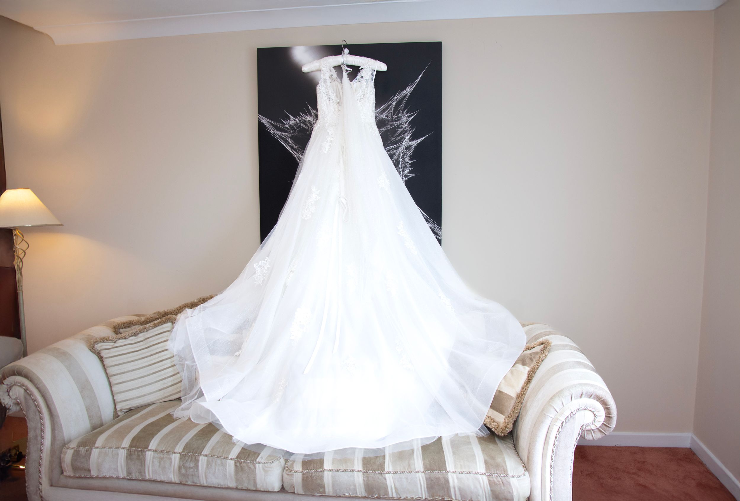 White wedding dress displayed on striped sofa against black and white wall art.