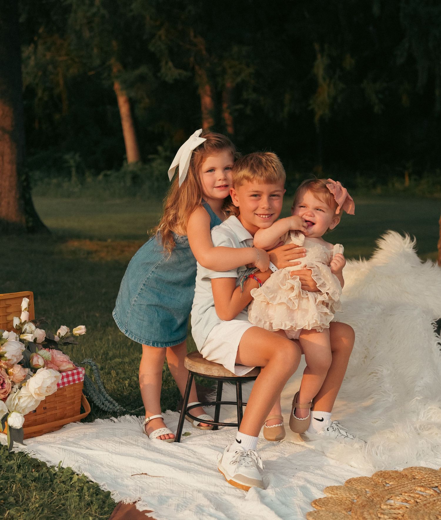 Children sitting together on a white blanket during an outdoor sunset photo session.