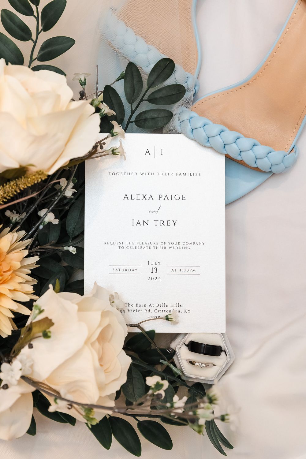 Wedding invitation suite with white roses and greenery on a light blue background.