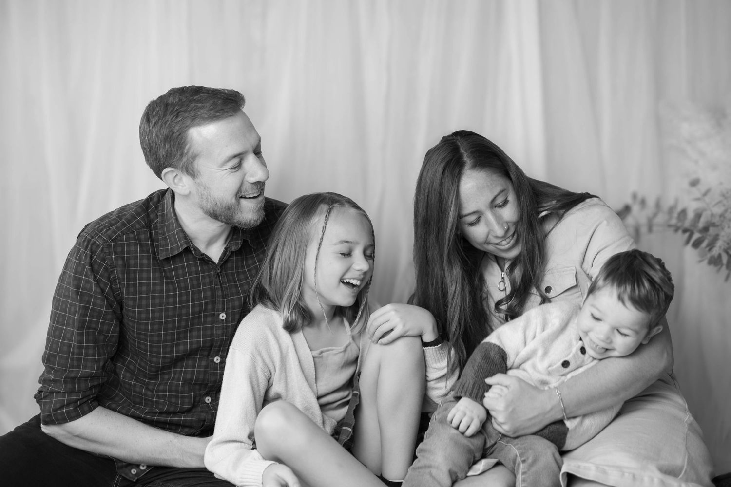 A candid black and white family portrait shows joyful interaction between loved ones on a couch.