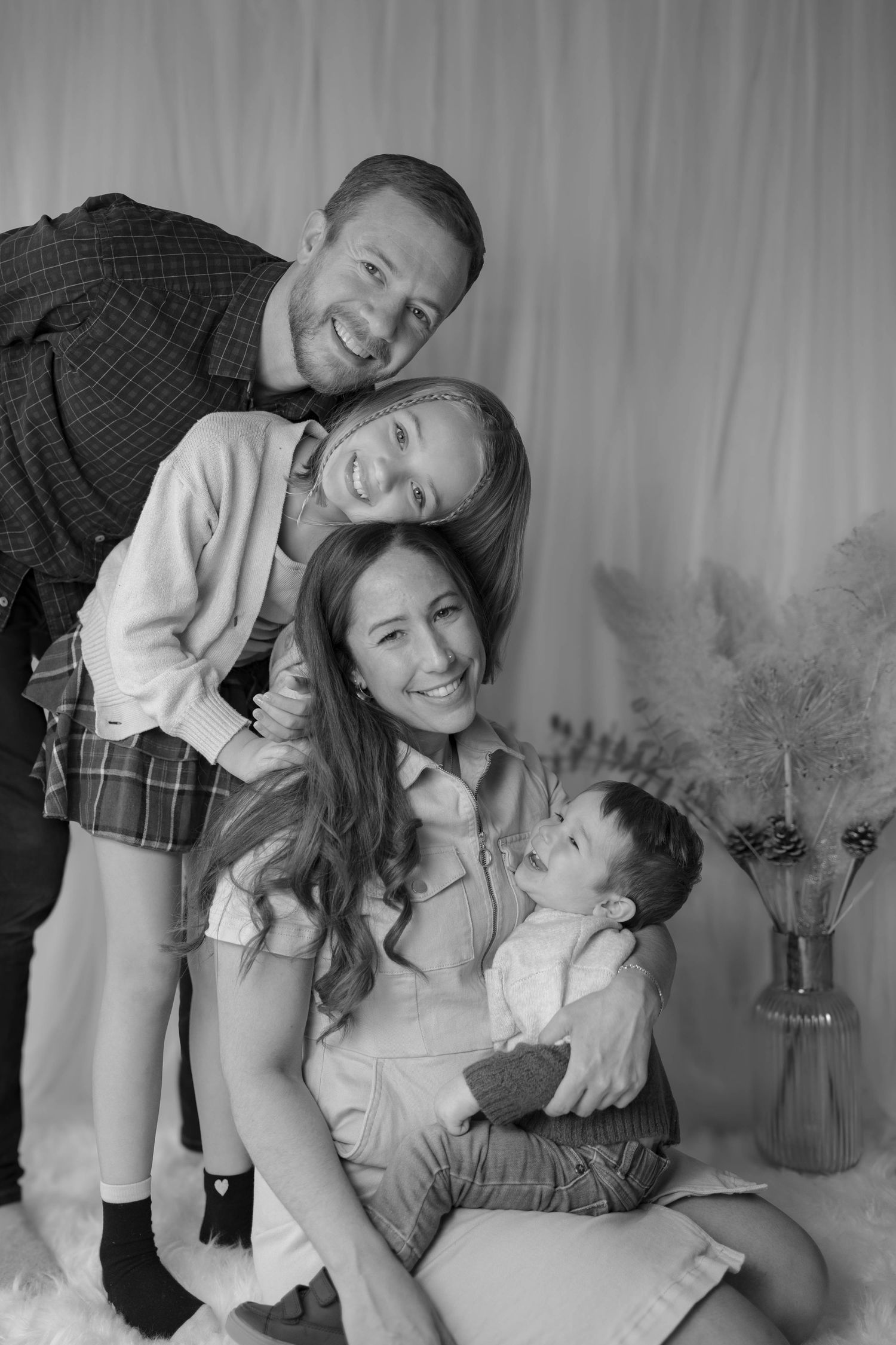 Black and white portrait of family posing together with decorative vase in background.