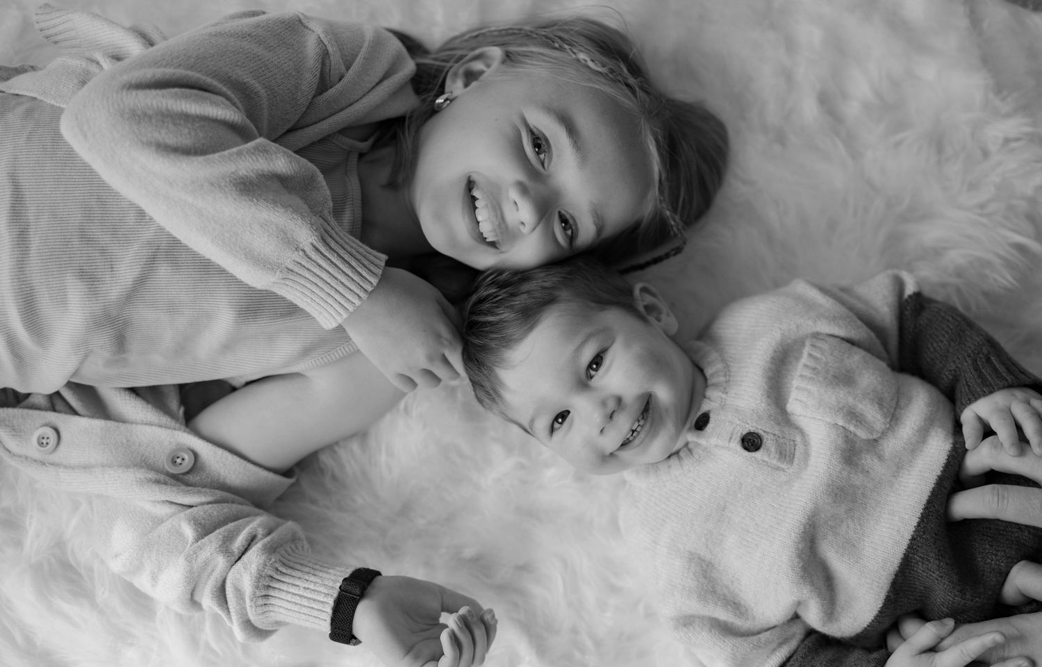 Black and white photo of siblings lying down and laughing together.