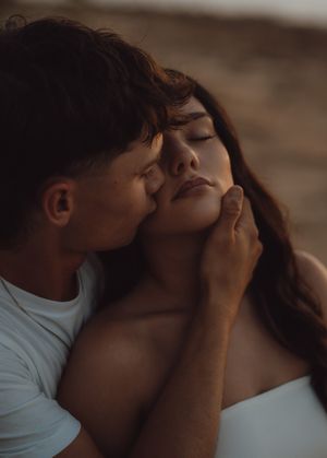 A tender couple shares an intimate moment, with a man gently kissing a woman's cheek while cradling her face.