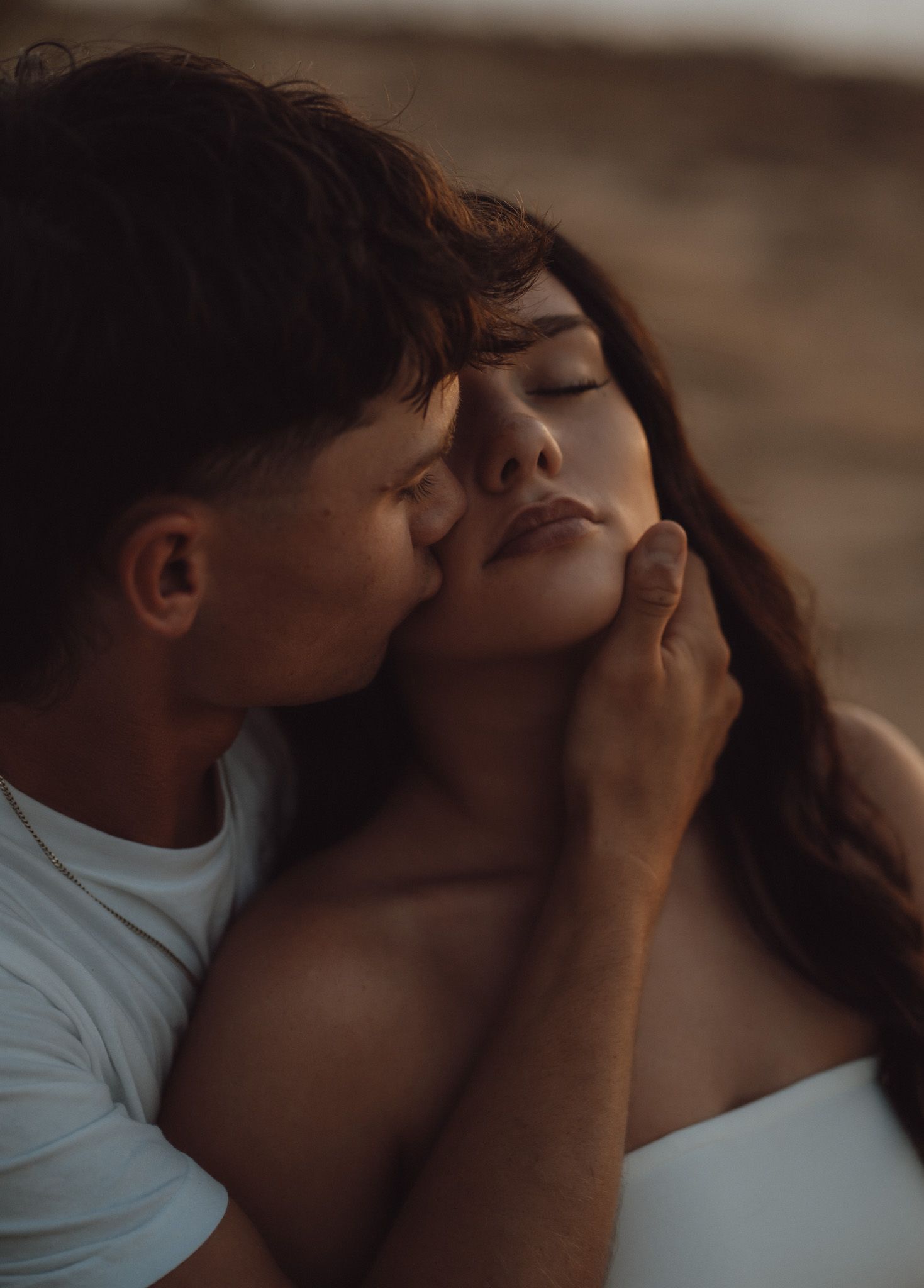 A tender couple shares an intimate moment, with a man gently kissing a woman's cheek while cradling her face.