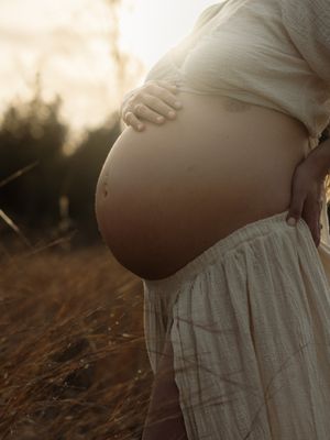 Pregnant woman in white dress cradling her bare baby bump in a golden field at sunset.