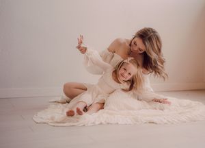 A person in a flowing cream dress poses gracefully on a light colored floor in a romantic boudoir setting.