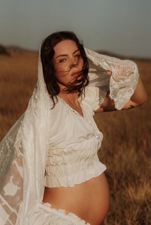 Pregnant woman in white crop top and veil poses gracefully in golden field during maternity photoshoot.