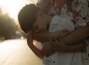 A child tenderly embraces an adult in warm golden sunlight on a blurred outdoor background.