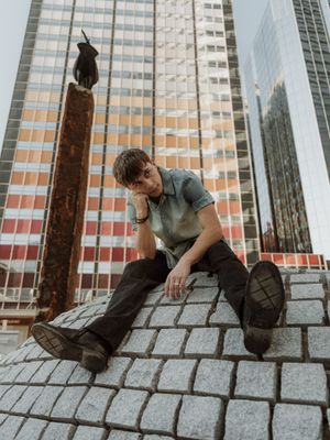 Young man sitting on cobblestone steps in urban setting with modern glass skyscrapers in background.