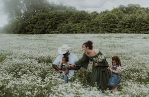 Family of four enjoying a sunny day in a blooming white wildflower field with lush green trees in background.