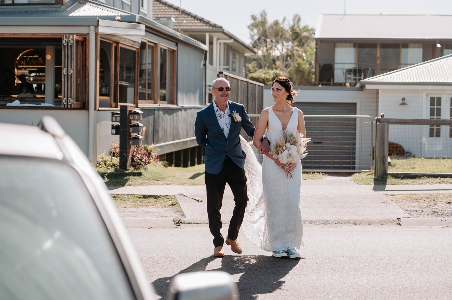 Wedding couple walking together on a sunny street with coastal buildings in the background.