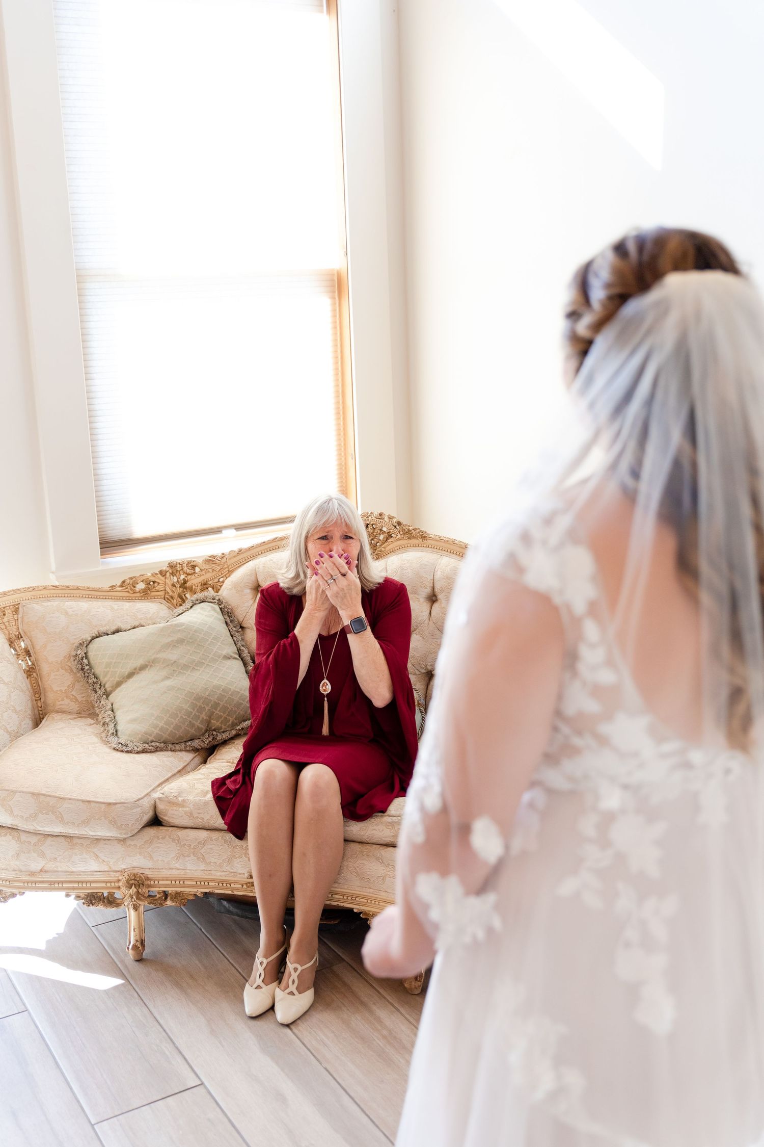 Emotional first look moment between bride and mother on vintage couch.