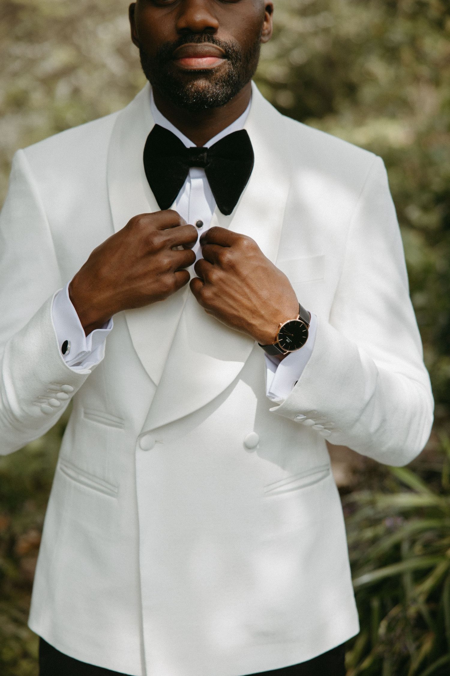 Elegant white tuxedo jacket with black bow tie shown in detail against natural background.