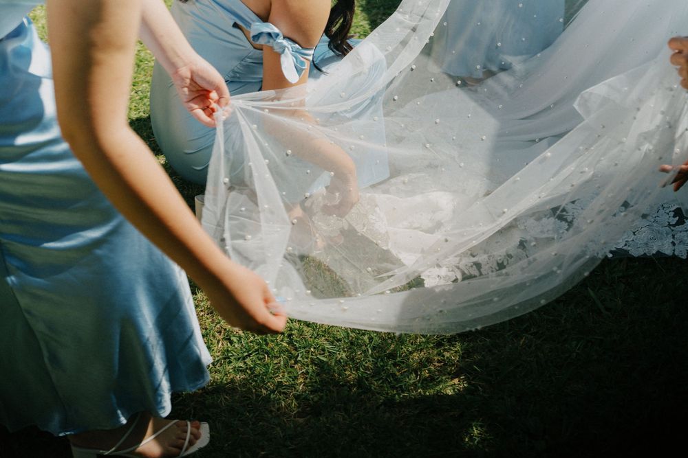 Close-up shot of delicate white wedding veil being adjusted on green grass.