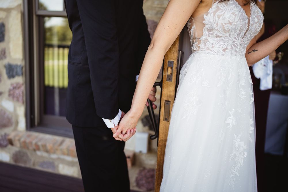 Close-up shot of a couple holding hands, with the bride wearing a white lace dress.