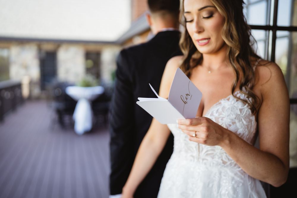 A bride in a white lace dress reads from a paper on an outdoor deck.