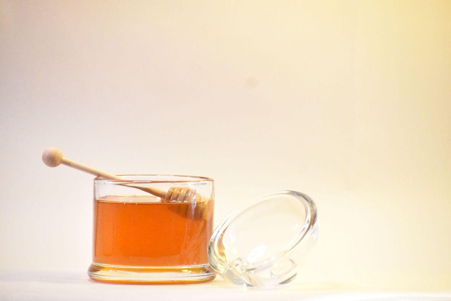 A jar of golden honey with a wooden dipper on a light background.
