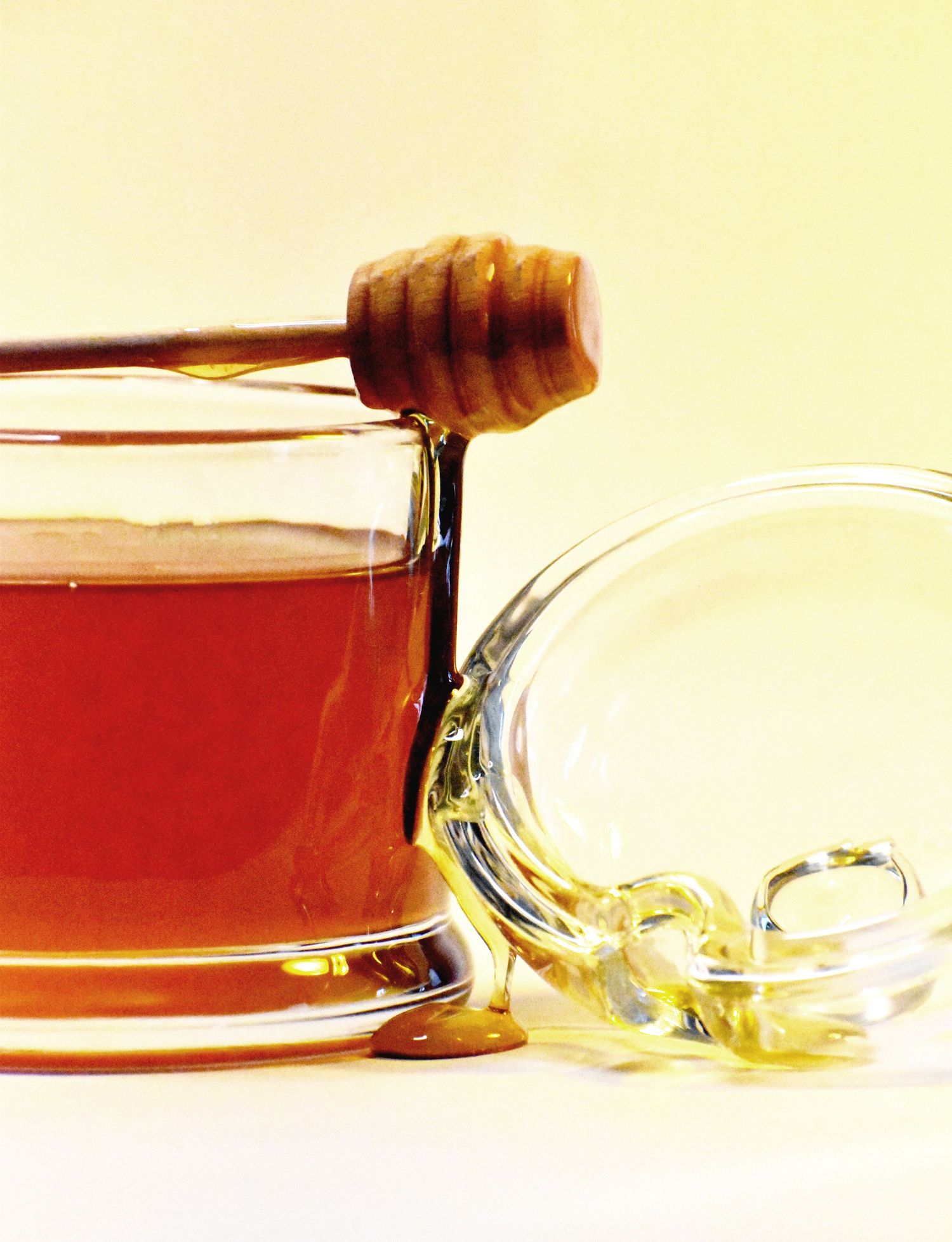 Close-up of honey being drizzled from a wooden dipper into a glass container.