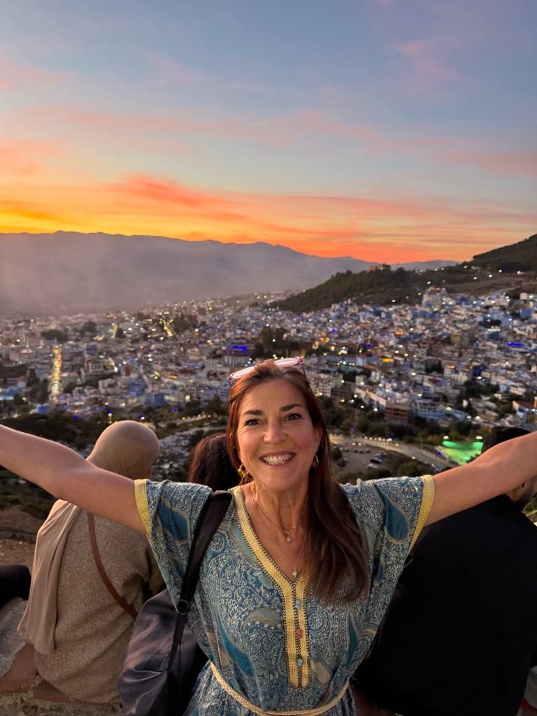 Happy woman with arms outstretched at sunset overlooking the blue city of Chefchaouen, Morocco.