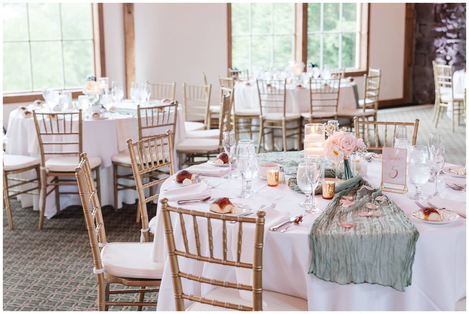 Elegant wedding reception tables set with light pink linens, chiavari chairs, and sage green table runners and florals.